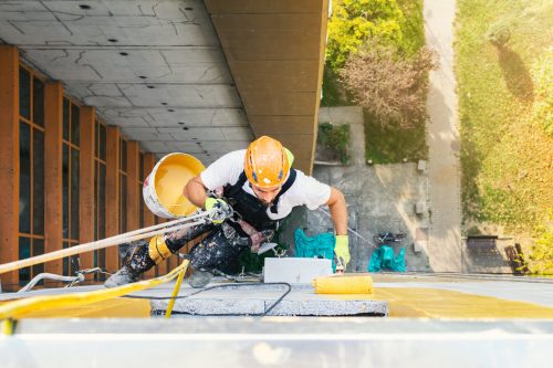 Hard hat worker paints wall while tethered
