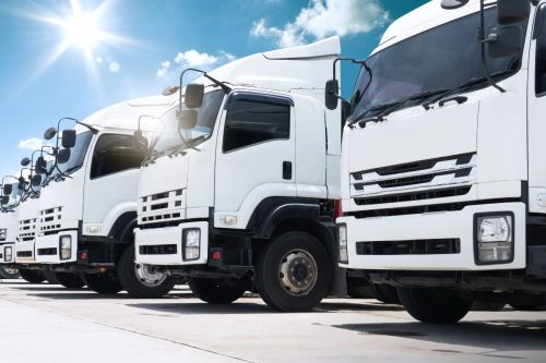 Line of commercial trucks on a concrete lot with a sunny sky, highlighting the concern can a wheel bearing cause vibration.